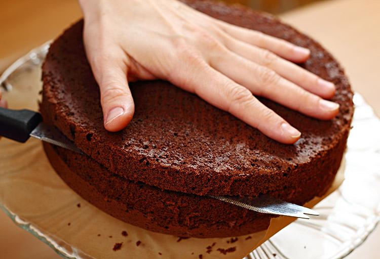 Mão de homem, cortando bolo de chocolate com uma faca.