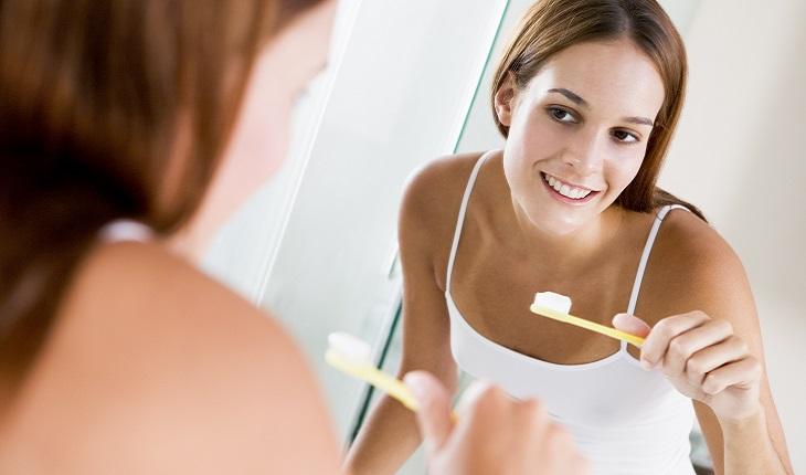 A foto mostra uma mulher em frente ao espelho escovando os dentes. Realizar essa atividade com a mão invertida ajuda a exercitar o cérebro