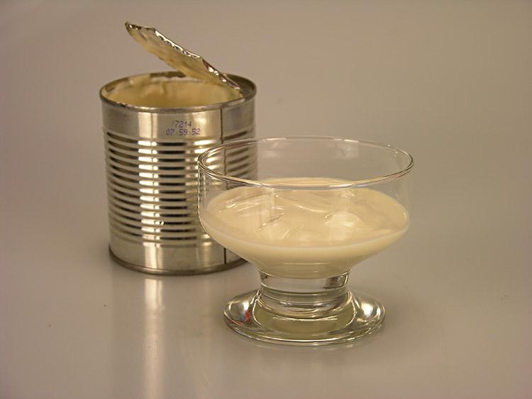Foto de uma lata de creme leite aberta com uma taça com um pouco de creme de leite.