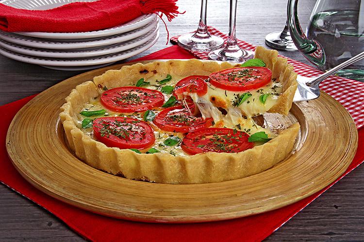 Torta-pizza em um prato de servir com uma fatia sendo retirada e pratos empilhados ao fundo.