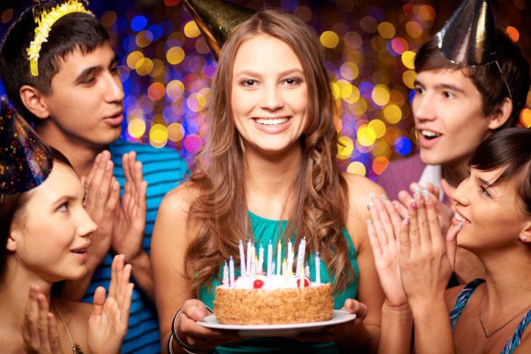 uma moça com um bolo na mão e várias outras moças cantando parabéns
