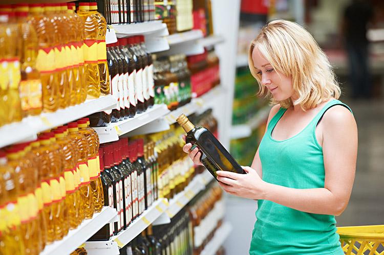 Mulher no supermercado olhando as prateleiras, segurando um azeite e analisando o produto.