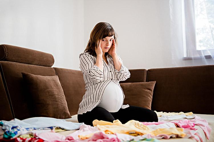 mulher-gravida-estressada-sentada-com-roupas-de-bebe