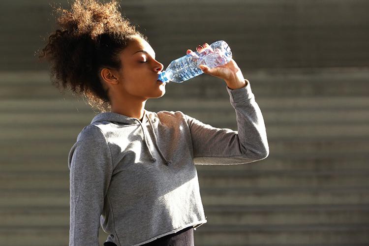 mulher com roupa de ginástica bebendo água para eliminar calorias 