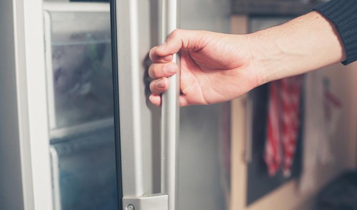 mão abrindo porta de uma geladeira