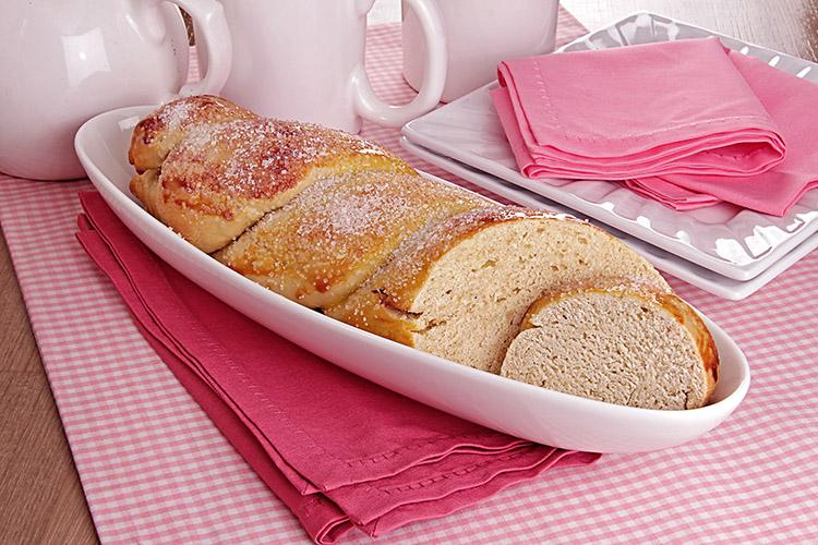 Pão de açúcar em um travessa branca com algumas fatias cortadas sobre uma toalha rosa com bulês ao fundo.