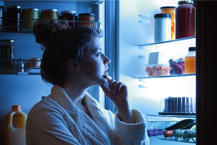 Mulher olhando alimentos na geladeira pensando o que comer na ceia