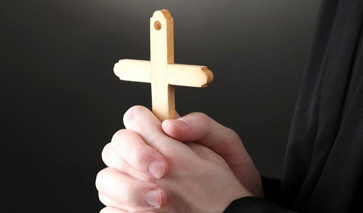 A foto mostra um padre segurando uma cruz de madeira, um dos objetos utilizados em um ritual de exorcismo