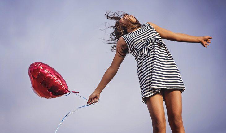 mulher de braços abertos sorrindo e seguand um balão em formato de coração
