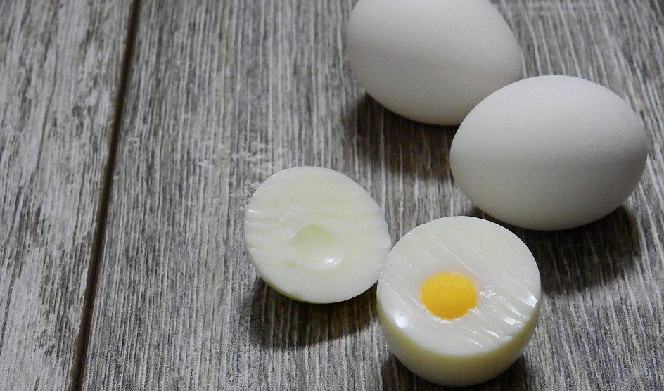 Marmita. Na foto, três ovos em cima de uma mesa de madeira. Um dos ovos está cozido e cortado ao meio, os outros dois com casca