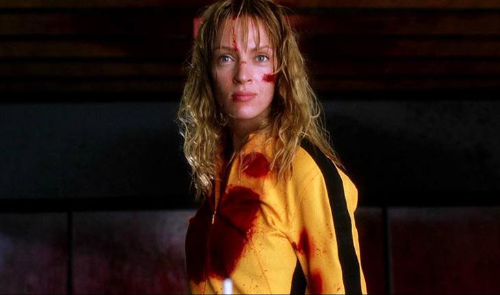 Uma Thurman veste a roupa de Kill Bill, amarela com uma faixa preta nos braços, manchada de sangue na altura do peito