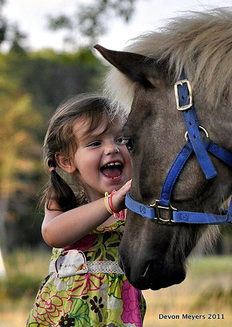 Menina sorridente fazendo carinho em cavalo