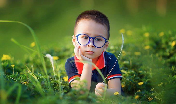 Dia das Crianças. Na foto, menino de óculos sentado na grama