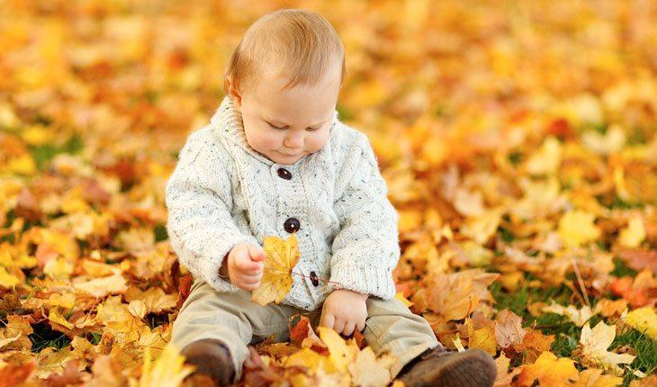 Dia das Crianças. Na foto, bebezinha com roupa de frio brincando com as folhas