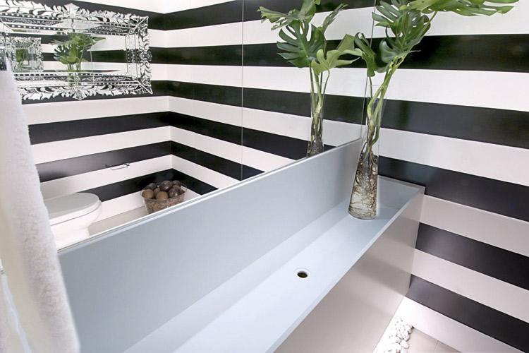 Banheiro pequeno decorado com papel de parede com listras horizontais e espelho grande