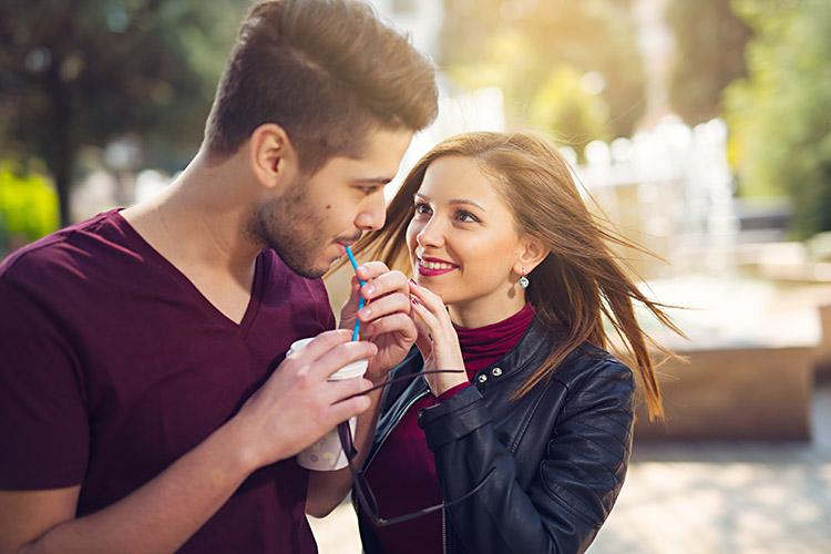 casal com olhar apaixonado, homem tomando uma bebida e mulher sorrindo para ele