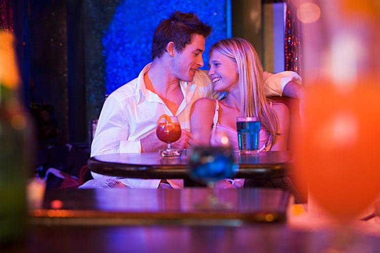 Casal se olhando sorrindo sentado em uma mesa bar