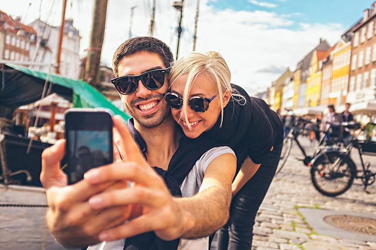 casal sorrindo e tirando selfie com o celular em uma rua