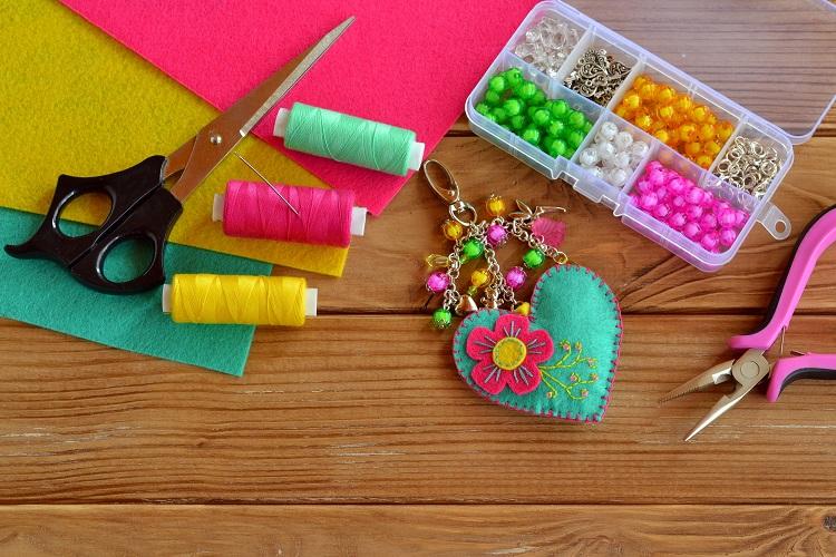 artesanato em feltro, peça de coração verde com flor e miçangas, linhas coloridas, tesoura e caixinha de miçangas