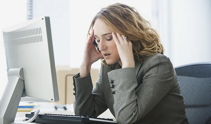 Na foto há uma mulher com as mãos na cabeça tentando se concentrar. Ela está trabalhando com um computador na frente
