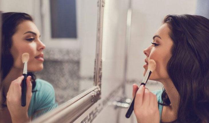 Mulher passando blush em frente ao espelho