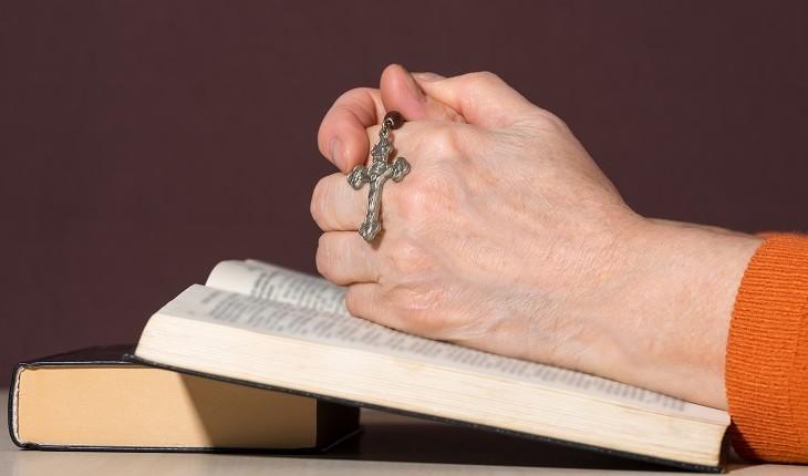 pessoa com as mãos sobre a bíblia segurando terço
