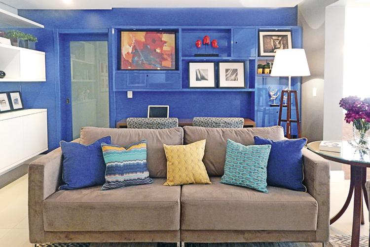 Sala com estante azul, sofá bege e almofadas coloridas