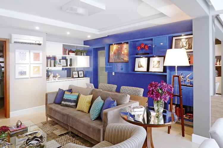 Sala com estante azul, sofá bege e almofadas coloridas