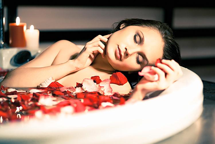 Mulher morena deitada em banheira, tomando banho de energia relaxante com pétalas de rosas vermelhas e brancas