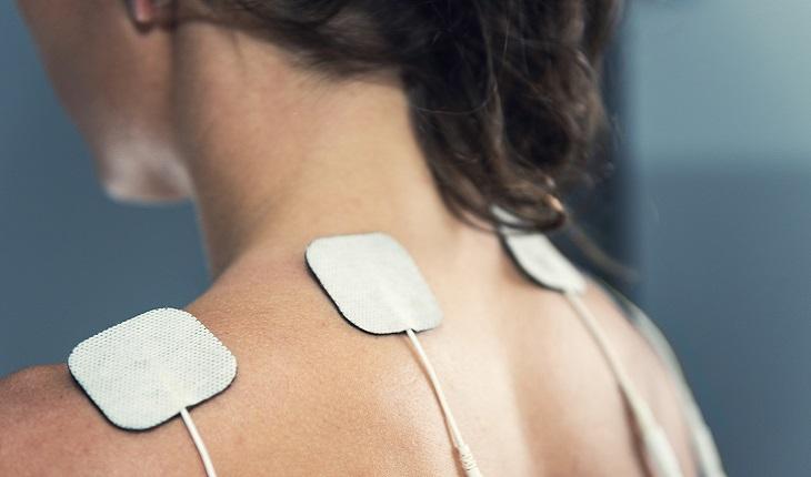 Na imagem, há uma mulher com eletrodos sobre o topo das suas costas, ilustrando a diatermia , uma das terapias eficientes contra artrite e artrose