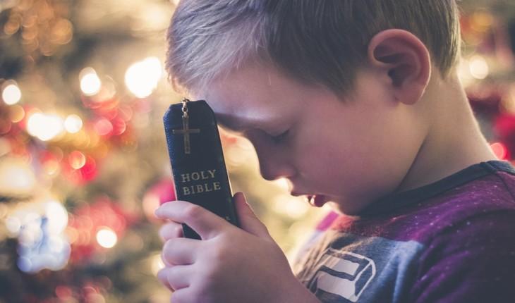 imagem de uma criança de olhos fechados, segurando uma bíblia encostada em sua testa. Provérbios da semana