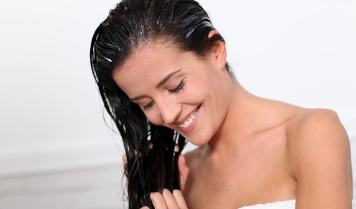 mulher com cabelo preto passando creme no cabelo molhado