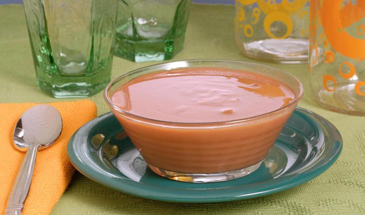 Imagem de doce de leite cremoso light, sobre um prato verde e dentro de uma vasilha de vidro. Ao redor da mesa alguns copos, uma colher e guardanapo laranja.
