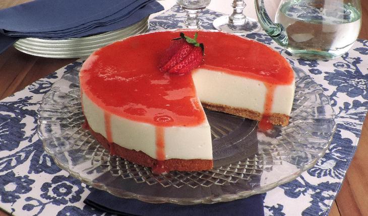 Imagem de um cheesecake de frutas vermelhas light, sobre um prato transparente. Na mesa outro prato decorativo.