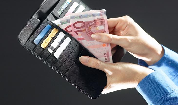 Sonhar com dinheiro - imagem de uma mão feminina vestindo uma camisa azul segurando uma carteira aberta e tirando de dentro duas notas de 10 euros.