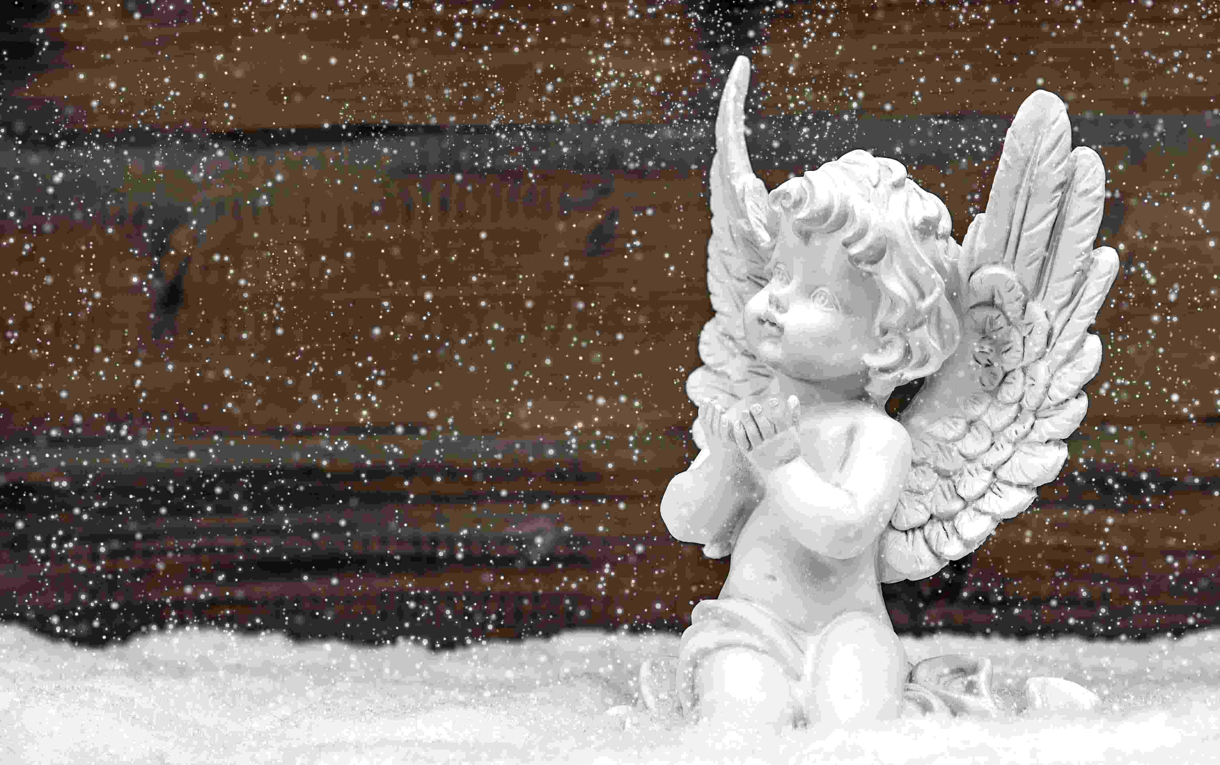 miniatura branca de um anjinho com as mão abertas em direção ao céu, neve caindo, fundo de madeira