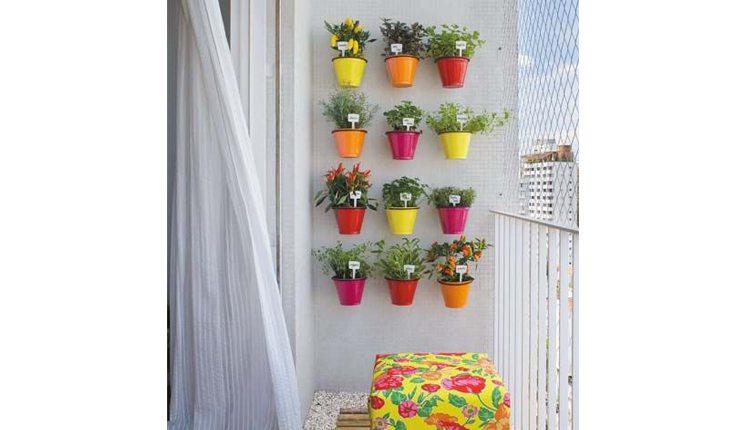 Na foto há um jardim vertical com vasos coloridos em uma varanda de apartamento.