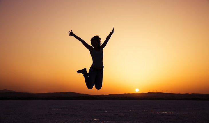 mulher feliz saltando com pôr do sol ao fundo