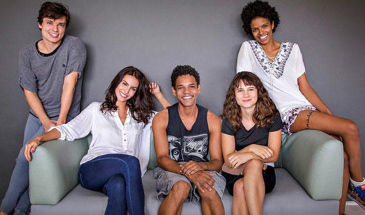Conteúdo Dublado. Na imagem há um sofá com três personagens da série brasileira 3% sentados e outros dois personagens em pé ao lado do sofá sorrindo