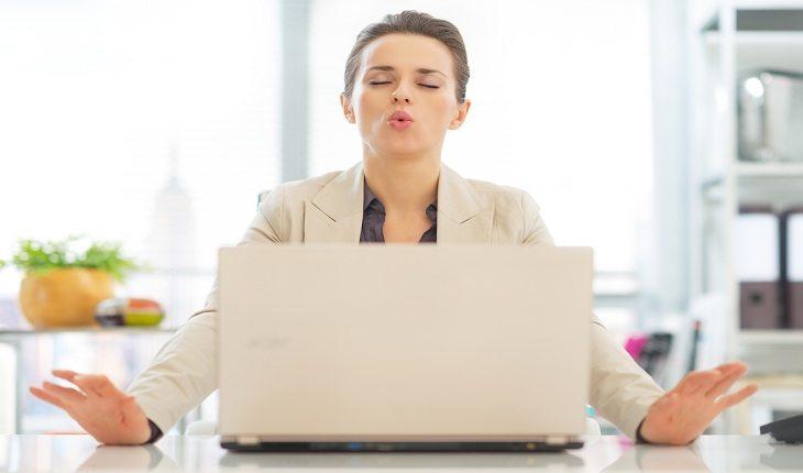 mulher sentada em frente a um notebook, de olhos fechados, tentando se concentrar