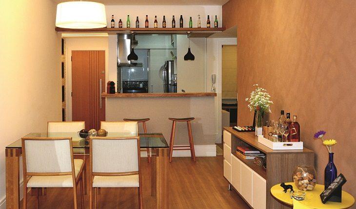 Entrada do apartamento com visual repaginado com copa e cozinha divididas por um balcão, todos os móveis de madeira na cor original e detalhes em branco.