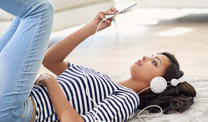 mulher deitada ouvindo música enquanto escreve no celular