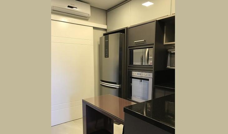 Foto de uma cozinha com armários escuros, mesa na cor berinjela e eletrodomésticos inox. Há uma porta de correr branca e um ar condicionado split