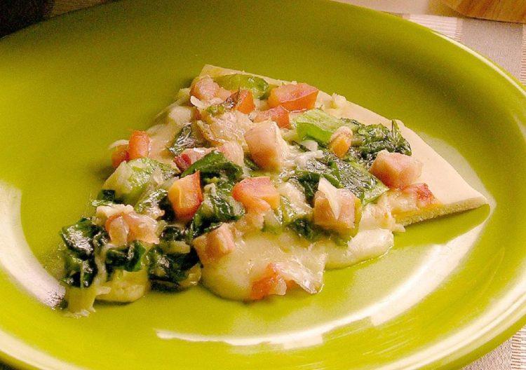 Pedaço de pizza de escarola. o queijo da fatia está derretido, e os ingredientes estão todos cobertos por ele. O pedaço está depositado em um prato verde. 