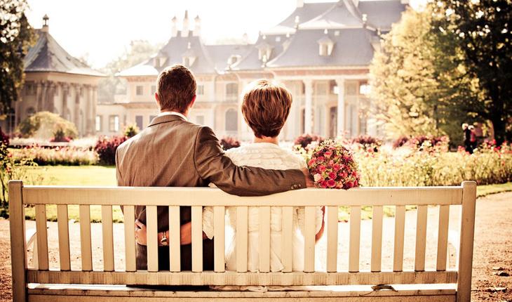 casal abraçado, sentado em um banco branco de madeira em um dia ensolarado