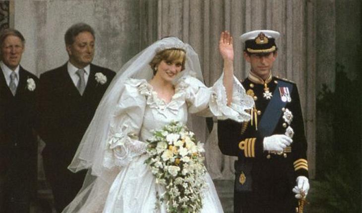 foto do casamento do príncipe Charles e da princesa Diana, eles estão saindo da igreja. Ela veste um vestido de noiva bufante, segura um buquê em cascata de flores branca e acena. Ele veste uma farda com muitas medalhas, quepe e luvas