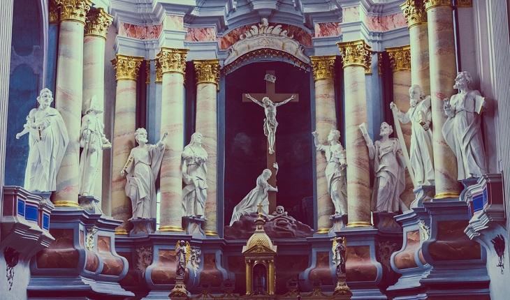 Na imagem, um altar está com várias esculturas de santos, no meio está jesus cristo crucificado. Novena de santa rita de cássia.