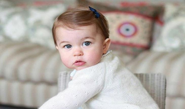 foto da princesa Charlotte bebê, vestindo um casaquinho branco e um lacinho preto na cabeça