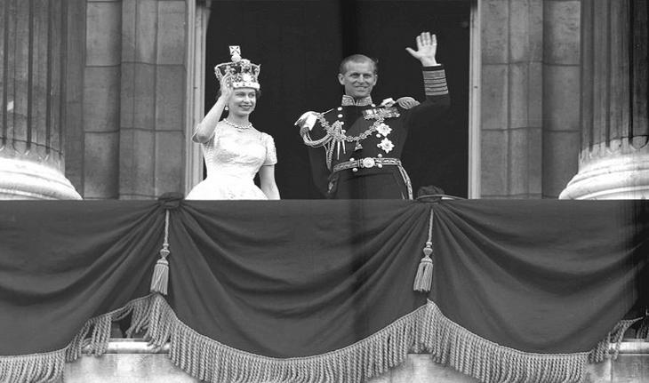 foto em preto e branco, antiga, da rainha Elizabeth e do príncipe Philip acenando em uma sacada