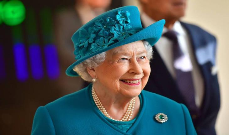 rainha Elizabeth sorrindo, usa uma blusa e um chapéu verde turquesa